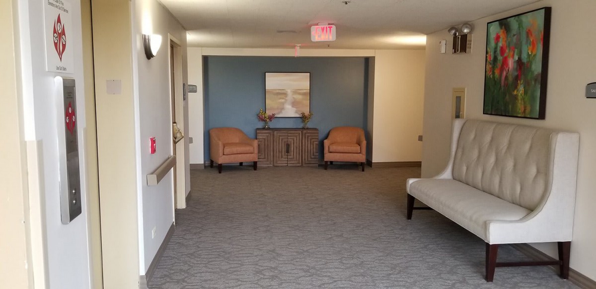 A quiet, well-furnished lobby with two chairs, a cabinet, and decorative artwork on the wall.