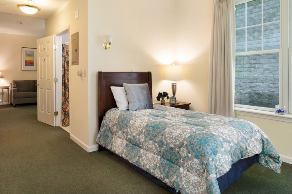 A cozy bedroom with a single bed adorned with a patterned quilt, accompanied by a nightstand and a wall-mounted lamp.