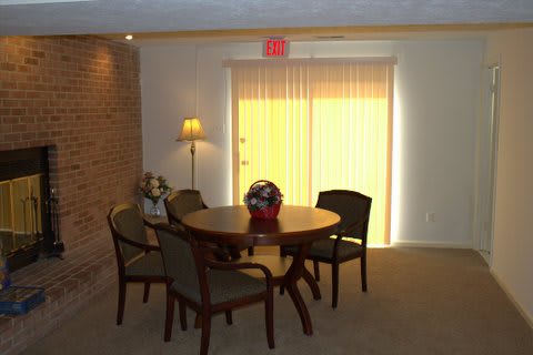 A cozy dining area with a round table and chairs, softly lit by a floor lamp beside window blinds.