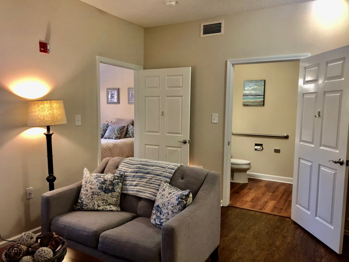A cozy living room with a sofa and decorative cushions, leading to a bedroom and bathroom.