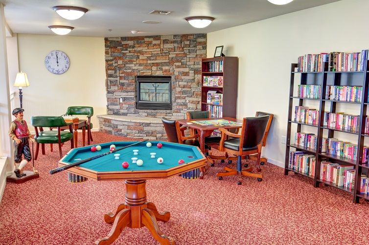 A cozy game room featuring a pool table, bookshelves, and a fireplace.