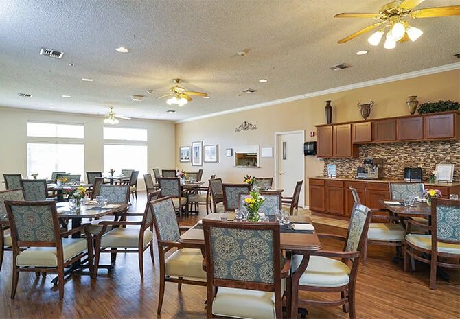A spacious dining room with elegant seating and a kitchen area in the background.