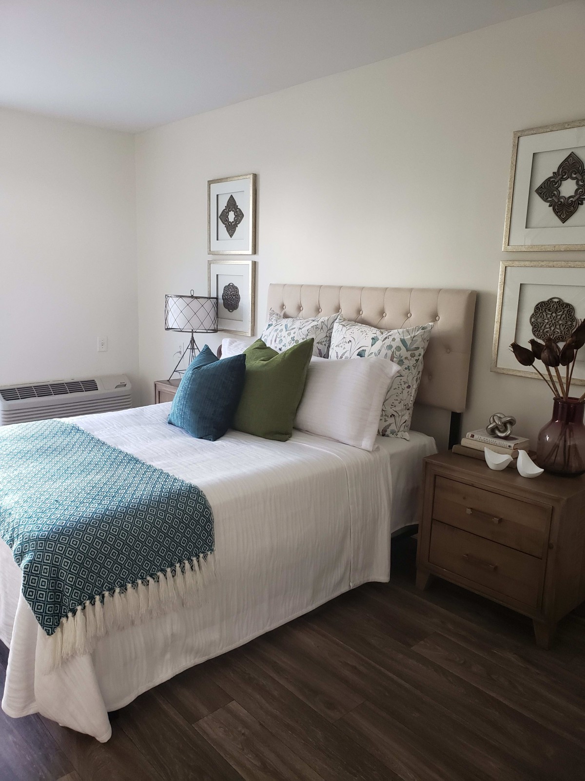 A cozy bedroom featuring a neatly made bed with decorative pillows and a textured blanket, accompanied by a stylish nightstand and wall art.