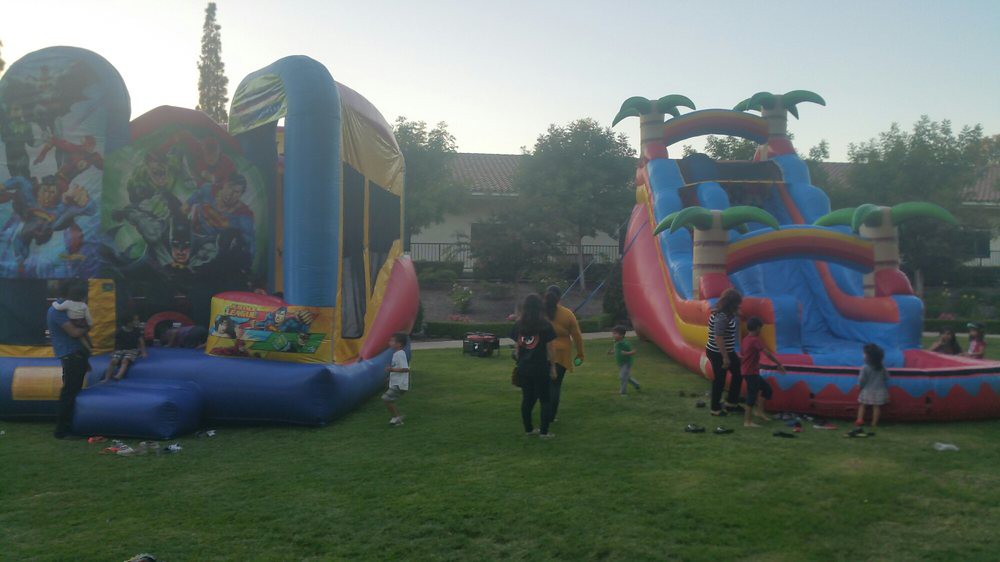 Children playing on an inflatable bounce house and slide at an outdoor event in a park.