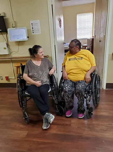 Two women in wheelchairs having a joyful conversation in a care facility.