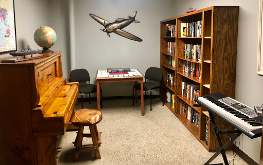 A cozy room featuring a piano, bookshelf filled with books, and a table set for games.
