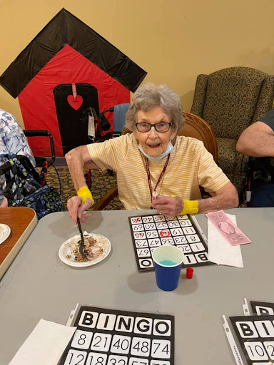 An elderly woman enjoying a game of bingo while having dessert at a community gathering.
