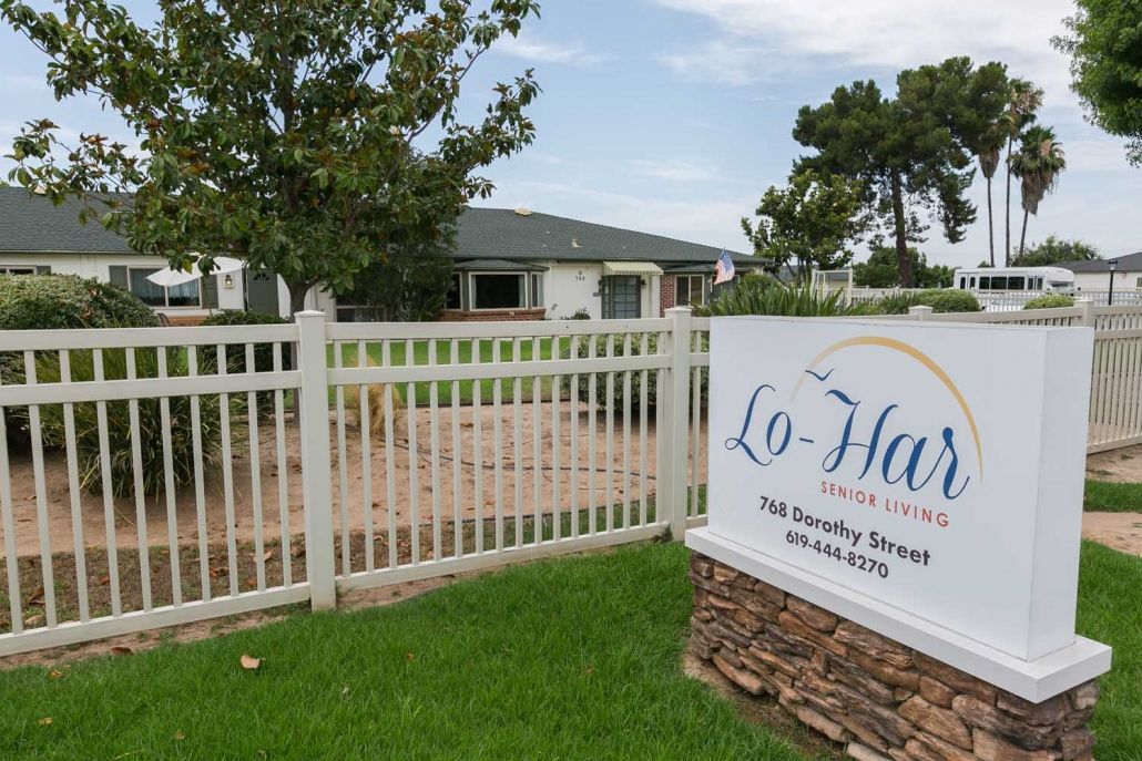 A fenced property with a building and a sign in front, surrounded by trees and grass.
