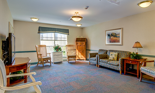 A cozy living room with rocking chairs and a sofa, featuring a large window and warm lighting.