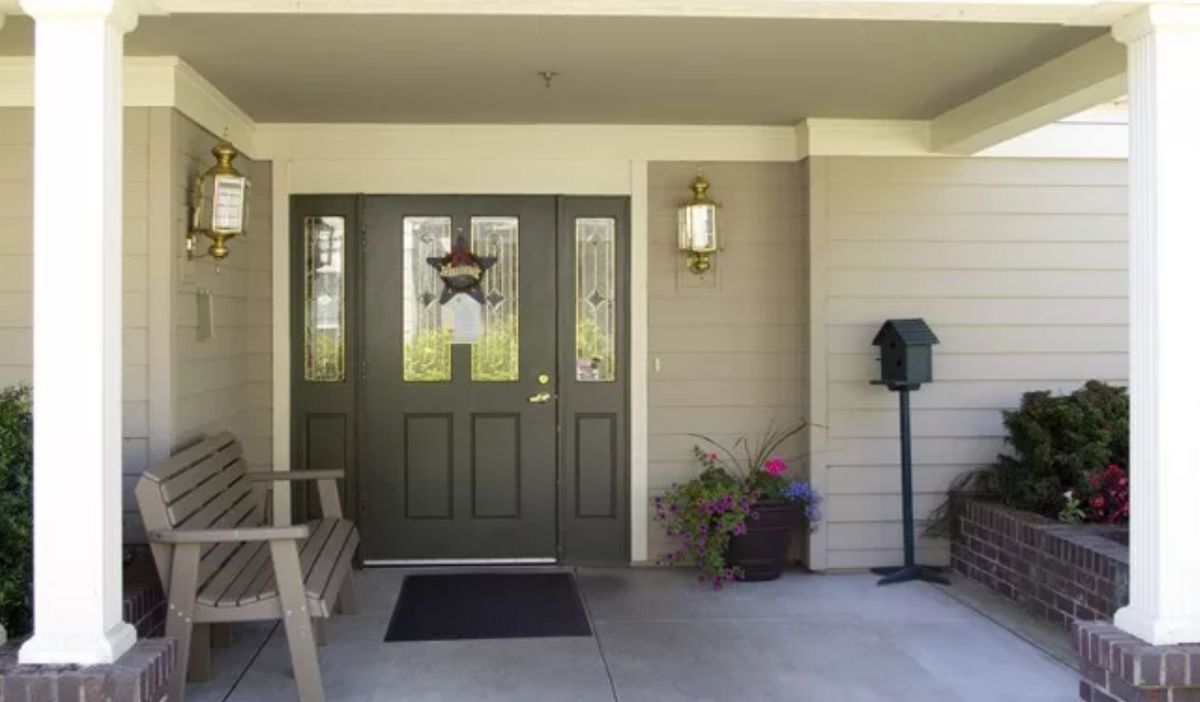 A welcoming front porch with a green door, outdoor seating, potted plants, and a mailbox.