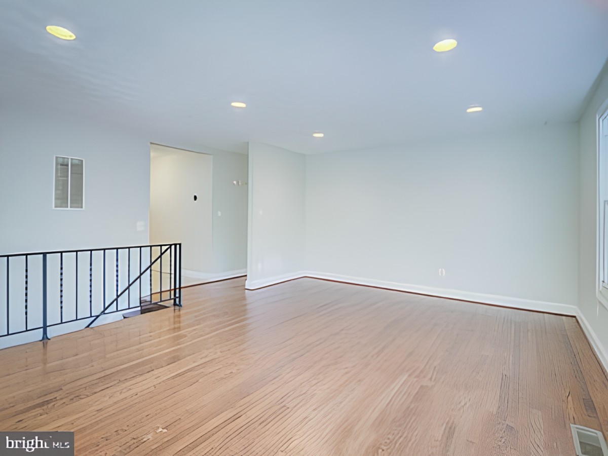 An empty room with hardwood flooring and white walls, featuring recessed lighting.
