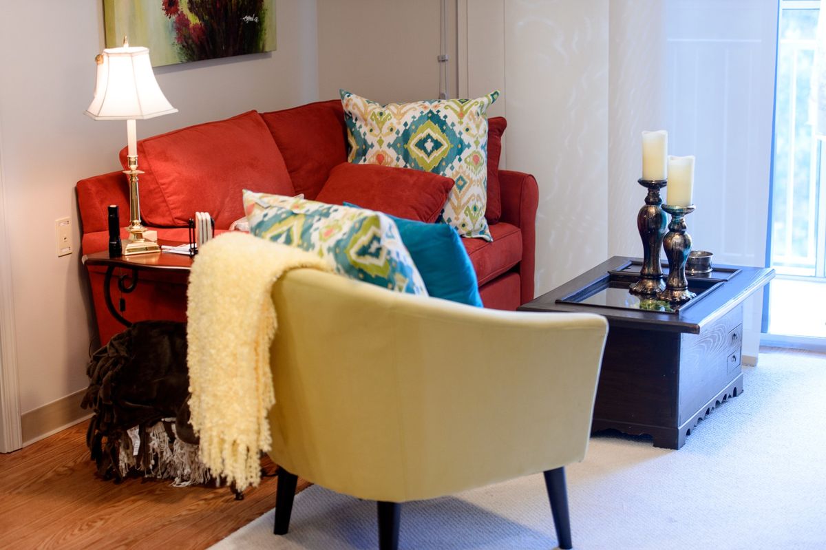 A cozy living room setup with a red sofa, decorative pillows, a beige armchair, and a side table adorned with a lamp and candle holders.