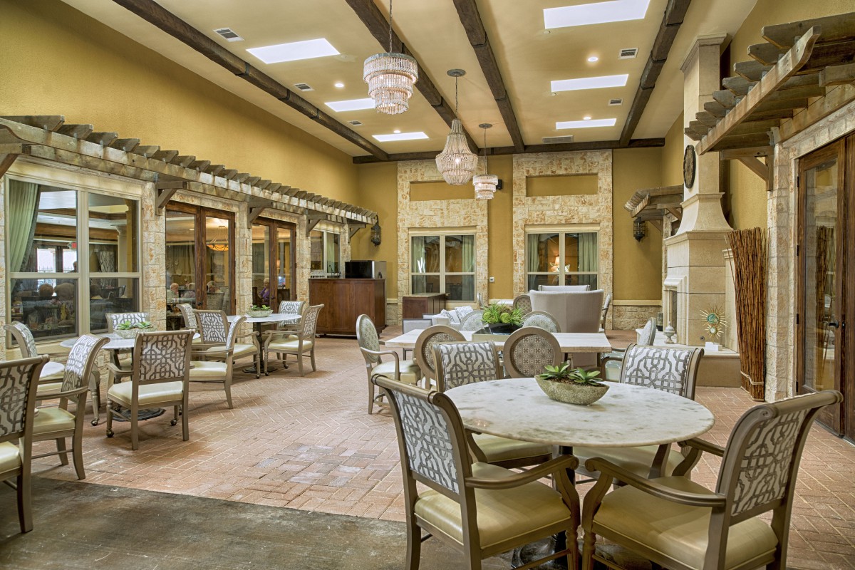 A spacious and elegantly decorated dining area with multiple tables and chairs, warm color tones, and decorative ceiling lights.