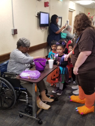 A heartwarming community event where children in costumes interact with an elderly woman in a wheelchair.