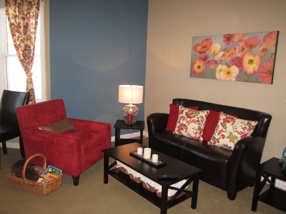 A cozy living room with a red armchair, black sofa with floral cushions, and a coffee table adorned with candles.