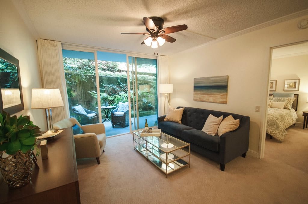 A cozy living room with a comfortable sofa, glass coffee table, and a view of the garden through sliding glass doors.