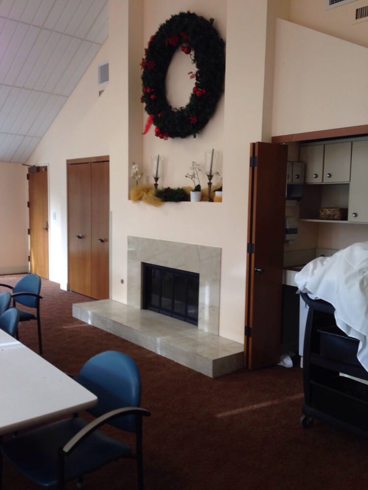 A cozy meeting room featuring a fireplace with a decorative wreath above it, surrounded by tables and chairs.