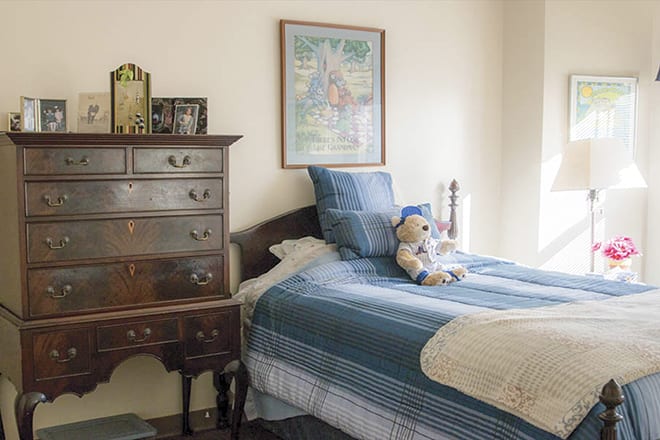 A cozy bedroom featuring antique furniture and a neatly made bed with a stuffed animal on top.