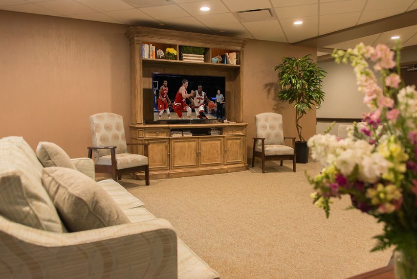 A cozy living room with a television, comfortable seating, and decorative plants.