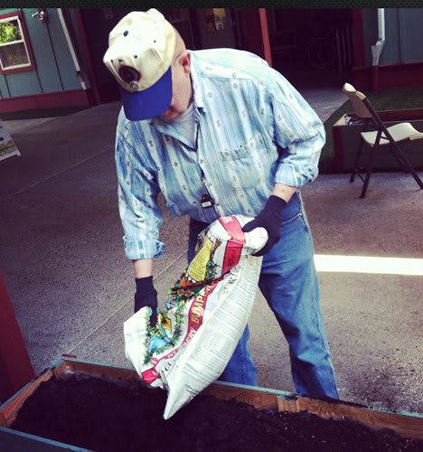 A person preparing soil by pouring it into a planter for gardening.