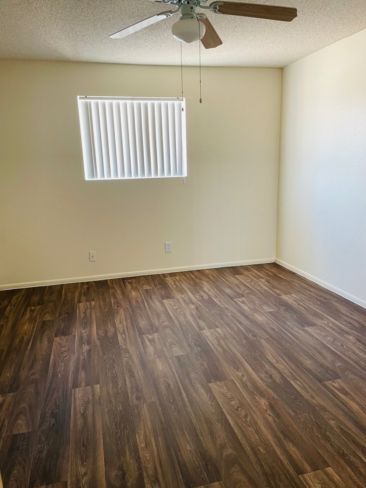 An empty room with hardwood flooring and a window with vertical blinds.