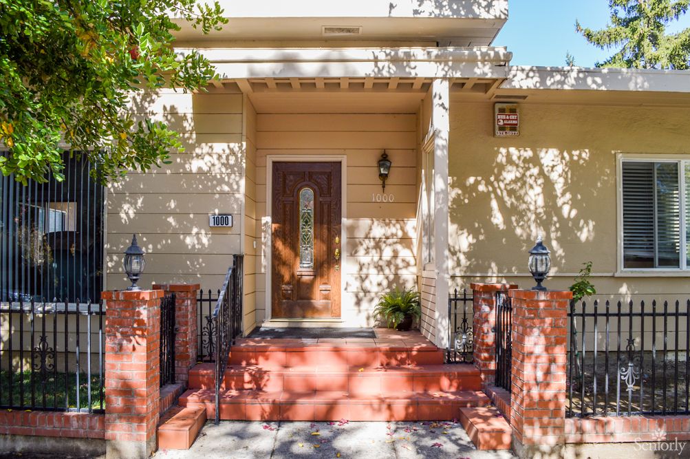 A quaint yellow house entrance with a wooden door and red brick steps adorned with outdoor lighting.