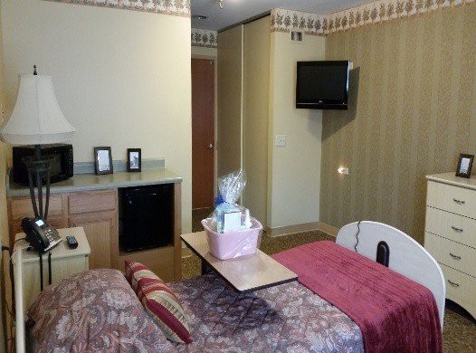 A hospital room featuring a bed with a gift basket, a wall-mounted television, and decorated walls.