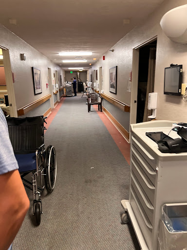 A healthcare worker navigating a hallway in a hospital, with medical equipment and wheelchairs visible.