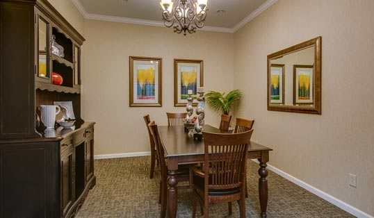 A warmly decorated dining room with a wooden table, chairs, chandelier, and vibrant wall art.