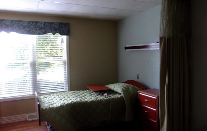 A minimalist bedroom with a single bed, dresser, and window with closed blinds.