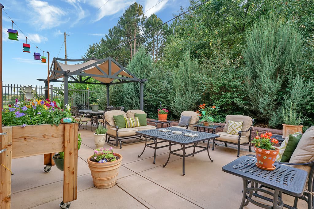 A cozy outdoor patio with cushioned seating and potted plants under a gazebo.