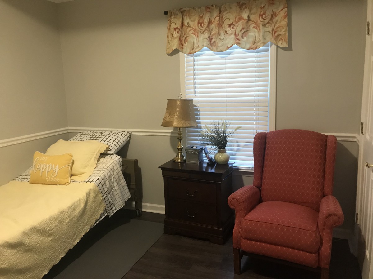 A cozy bedroom with a bed, pink armchair, nightstand, and window with curtains.