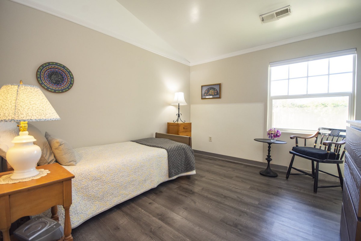 A minimalist bedroom with a single bed, lamp, and wooden flooring.