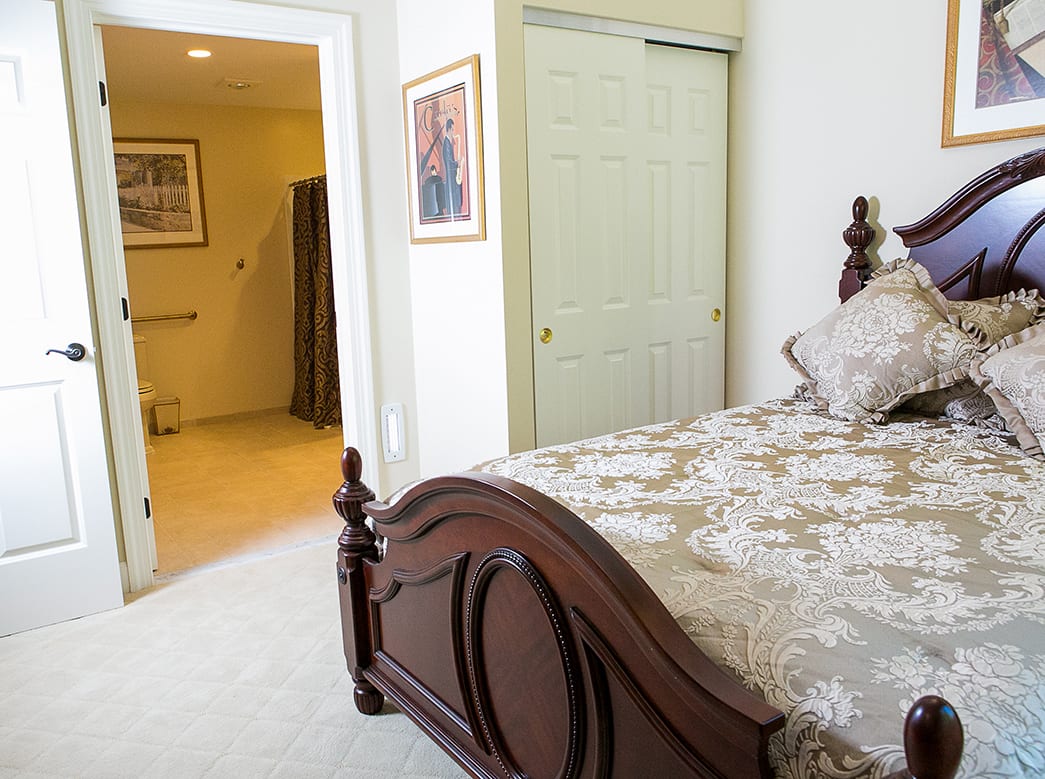 A cozy bedroom with a wooden bedframe and floral bedding, adjacent to an open bathroom door.