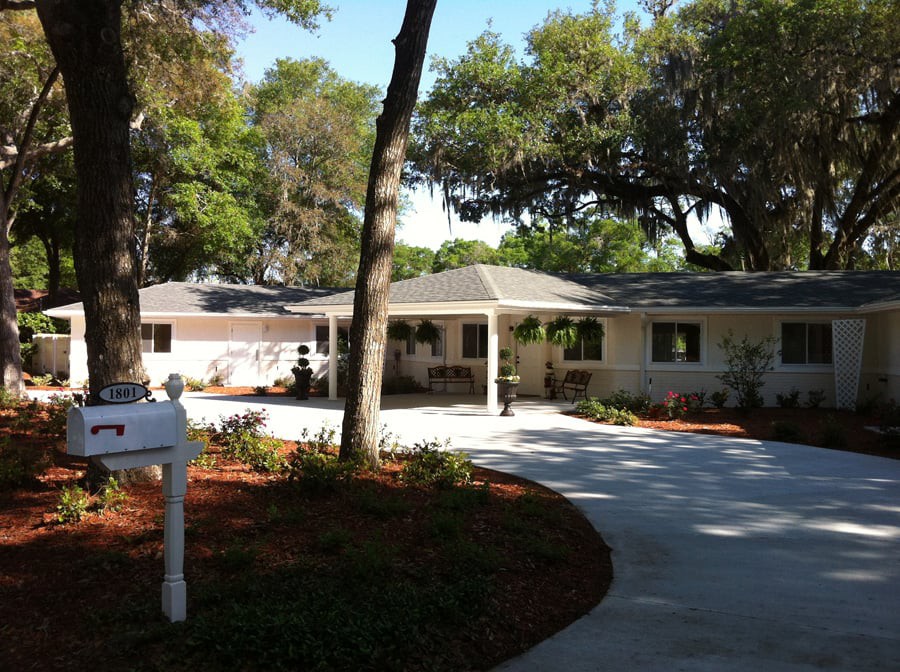 A charming single-story house with a curved driveway and surrounding trees.