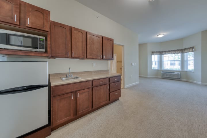 A modern apartment kitchen with wooden cabinets and a compact refrigerator.
