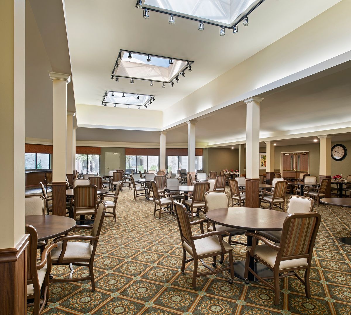 A spacious dining area with multiple tables and chairs, featuring elegant lighting and a carpeted floor.