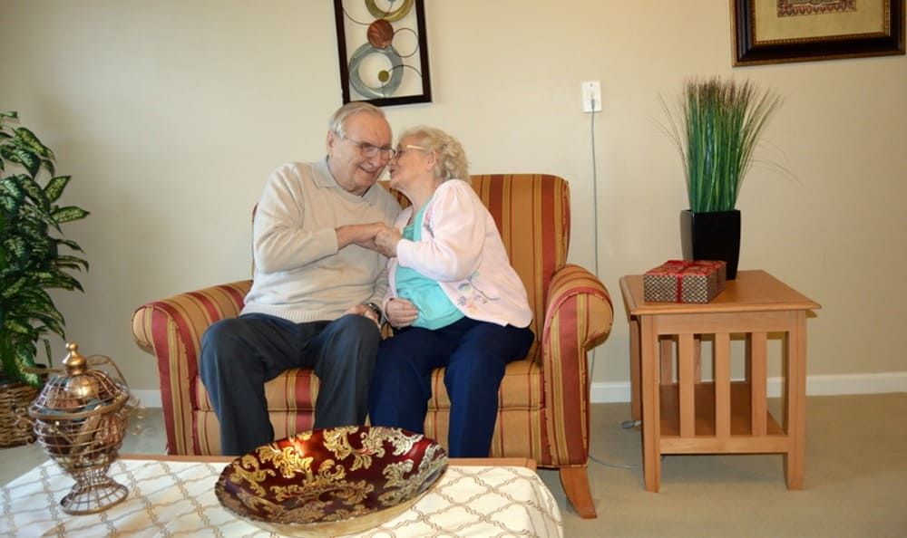 An elderly couple sharing a tender moment while seated in a cozy living room.