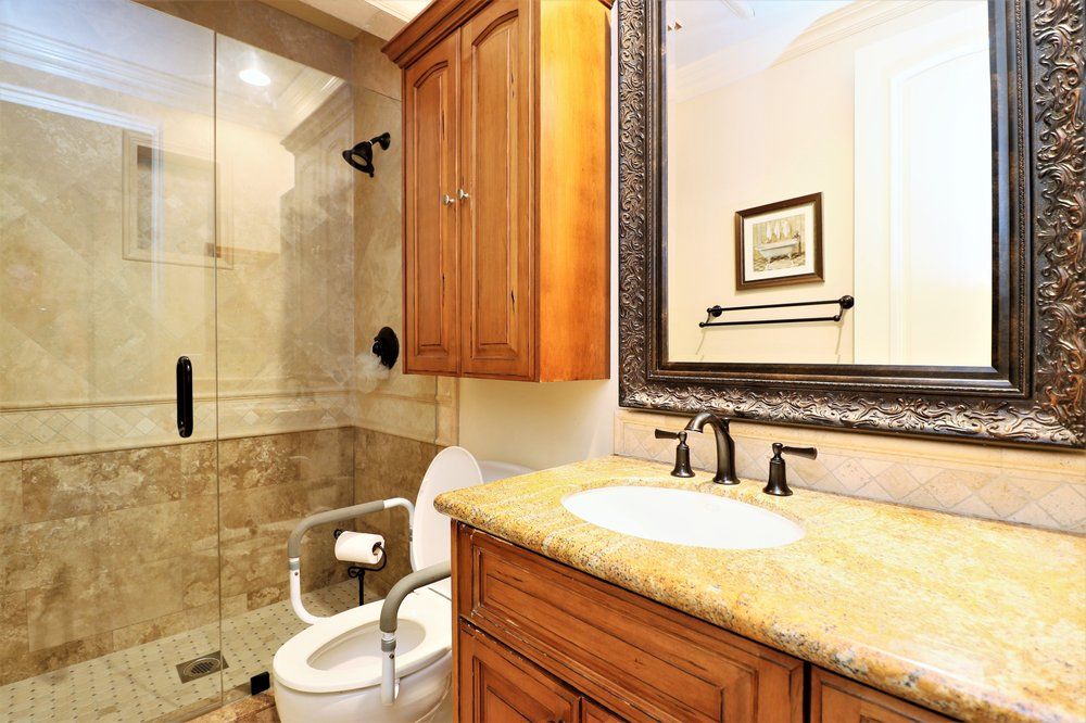 A well-lit bathroom featuring a wooden cabinet, a granite countertop sink, and a glass-enclosed shower.