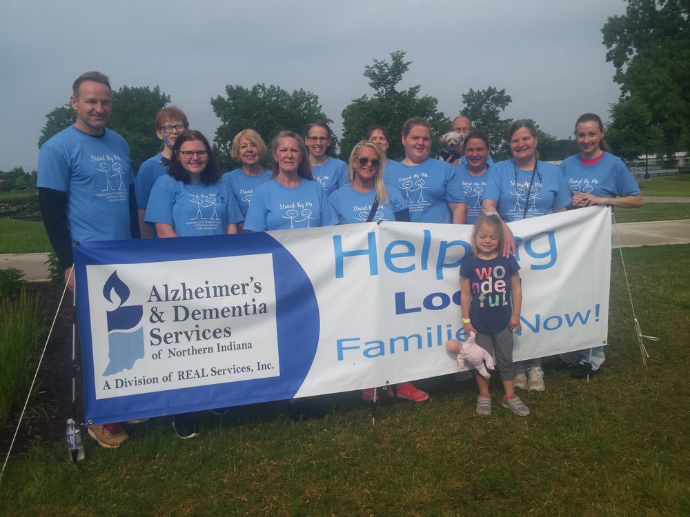 A group of people gathered outdoors wearing matching shirts, standing behind a banner promoting Alzheimer's and Dementia services.