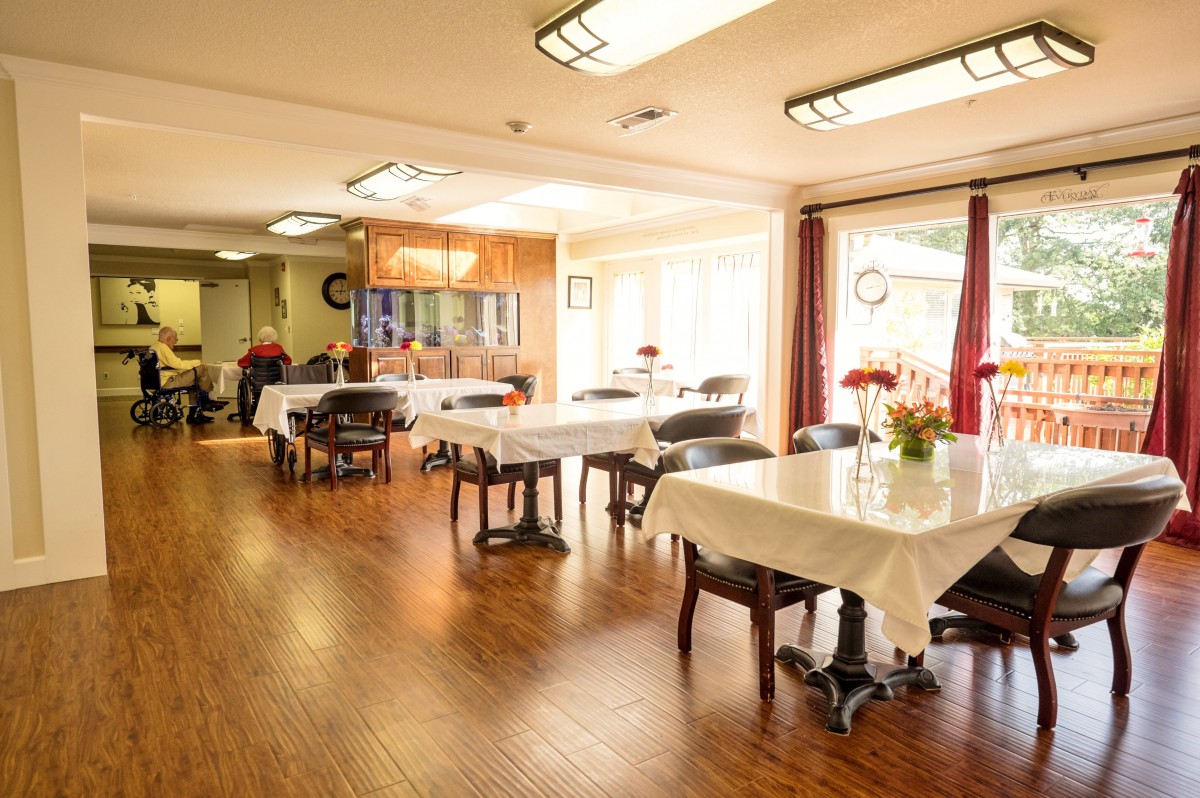 A bright dining room with neatly arranged tables and chairs, illuminated by natural sunlight.