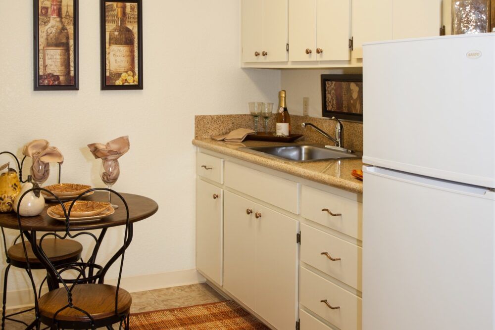 A cozy apartment kitchen with a small dining table and chairs, featuring cabinets, a sink, and a refrigerator.