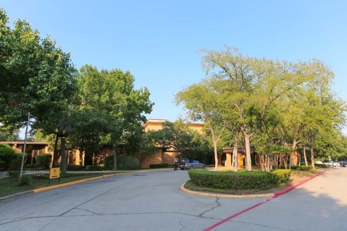 A building entrance surrounded by trees and a driveway under a clear blue sky.
