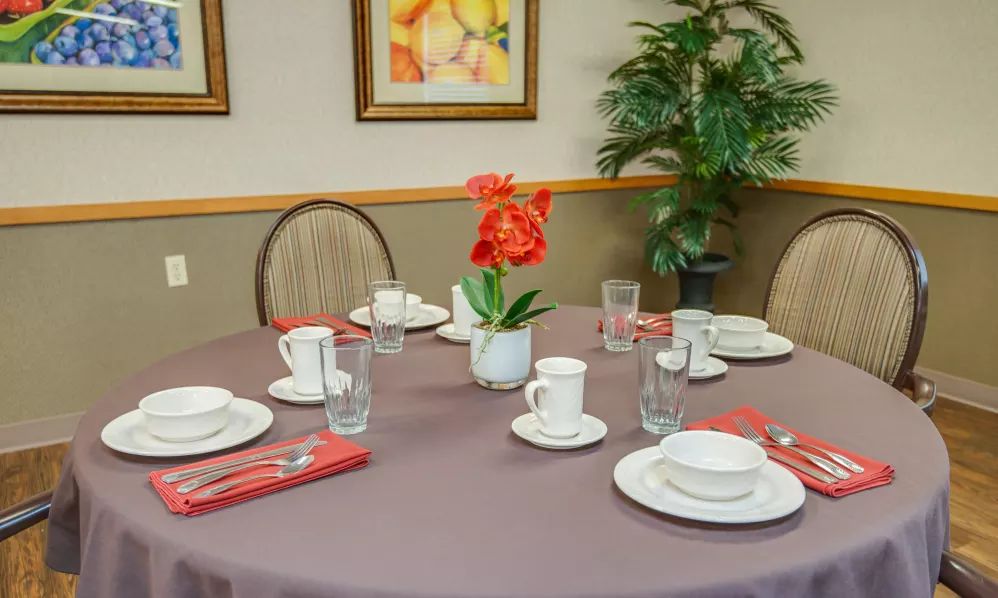 A neatly arranged dining table with place settings and a decorative flower centerpiece.