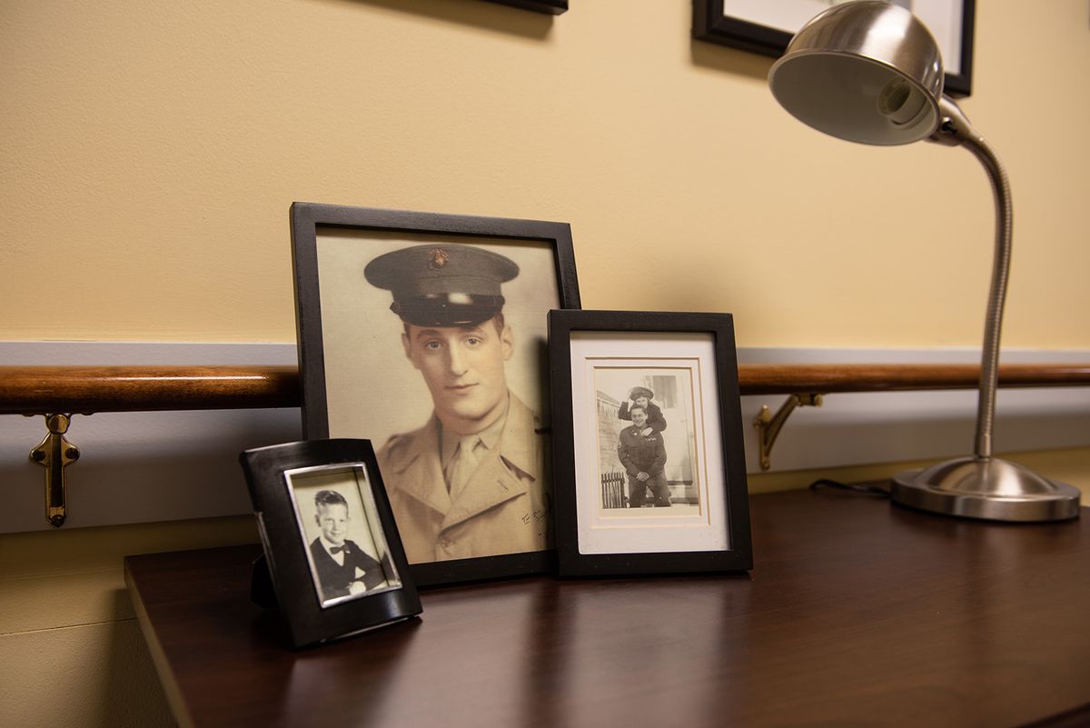 A collection of framed vintage photographs, including one of a person in military uniform, displayed on a desk with a lamp.