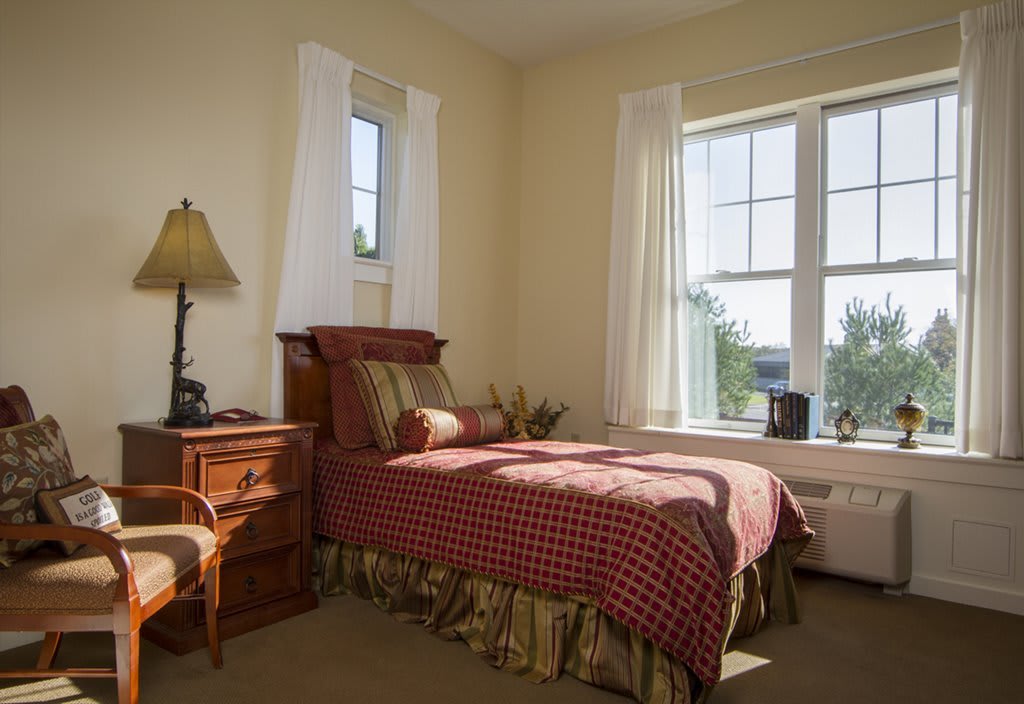 A cozy bedroom with a single bed and abundant natural light from large windows.