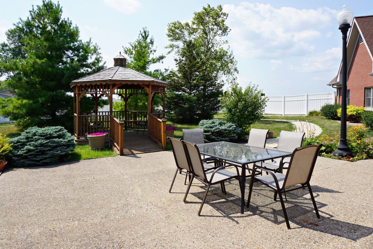A serene outdoor patio area with a glass table and chairs, adjacent to a charming gazebo surrounded by greenery.