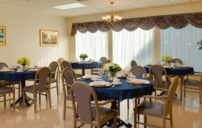 A well-lit dining room with neatly arranged tables and chairs, adorned with floral centerpieces.
