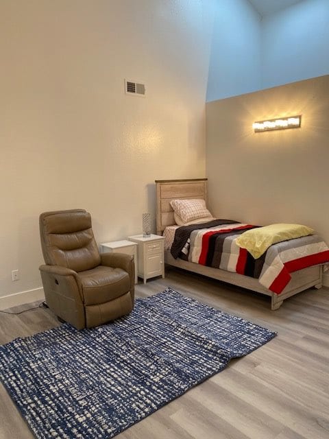 A minimalist bedroom featuring a single bed with a colorful blanket, a recliner chair, and a cozy rug.