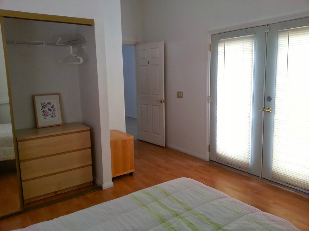 A minimalist bedroom interior featuring a dresser, open door, and window with natural light.